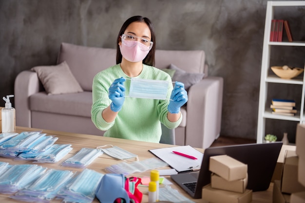 Photo d'une blogueuse d'affaires asiatique organiser les commandes Masques faciaux contre la grippe montrant le processus de caméra Web du produit prêt préparer les packs colis de livraison sécurité bureau à domicile quarantaine à l'intérieur