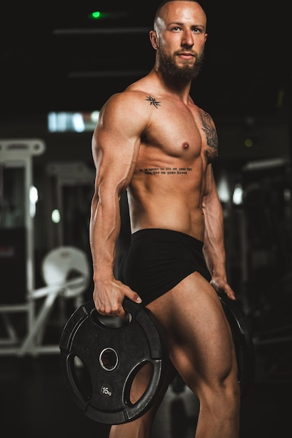 Photo d'un bodybuilder musclé montrant ses muscles parfaits après s'être entraîné avec une plaque de poids au gymnase.
