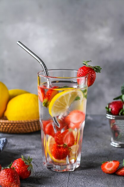 Photo d'une boisson fraîche glacée d'été rafraîchissante. Eaux infusées aux fraises. Eau minérale au citron fraises fraîches sur fond gris. Eau détox au citron fraise. Copiez l'espace.