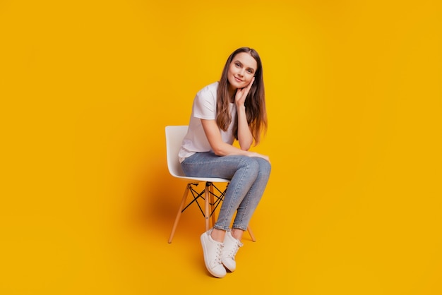 Photo d'une charmante dame assise sur une chaise à la joue portant un t-shirt blanc posant sur fond jaune