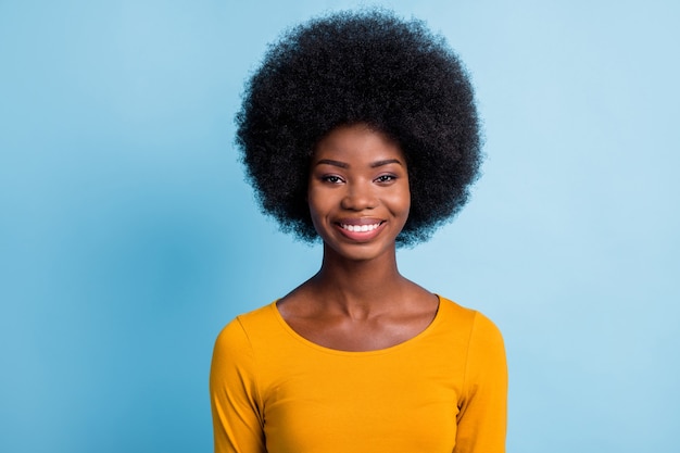 Photo d'une charmante jeune femme noire regarde la caméra à pleines dents souriante brillante porter une chemise jaune isolée sur fond de couleur bleu