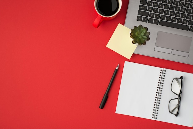 Photo ci-dessus d'une tasse de café pour ordinateur portable, d'un bloc-notes, d'un autocollant de lunettes et d'un stylo isolés sur le fond rouge avec espace vide