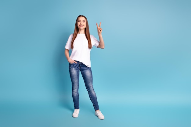 Photo complète du corps d'une jeune femme charmante montre des doigts paix vsymbol cool isolé sur fond de couleur bleue