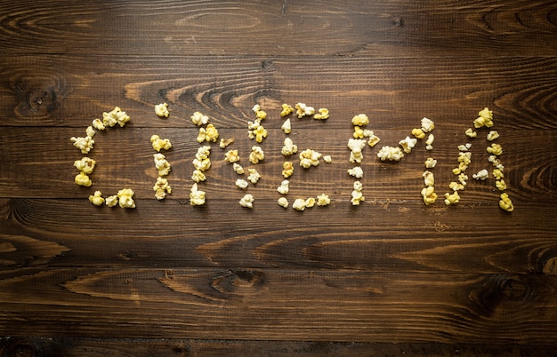 Photo conceptuelle du mot cinéma écrit par du pop-corn et des grains sur fond de bois