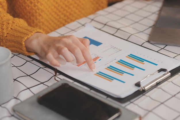 Photo coupée d'une femme d'affaires indépendante asiatique tenant une tasse de café et faisant la planification l'analyse du rapport financier le plan d'affaires l'analyse financière de l'investissement le lieu de travail