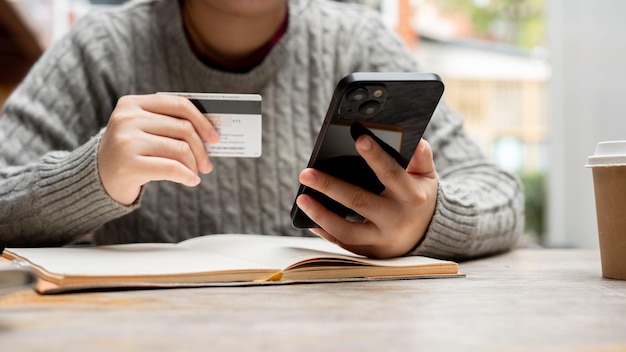Photo une photo coupée d'une femme tenant son smartphone et une carte de crédit assise à une table.