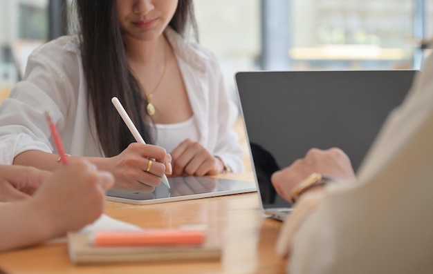 Photo coupée d'une femme utilisant un stylo pour écrire sur une tablette et des collègues au bureau