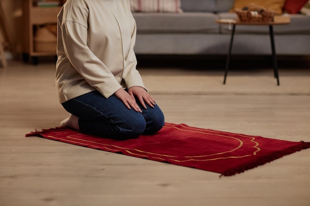 Une photo coupée d'une jeune femme en tenue décontractée agenouillée sur un petit tapis rouge