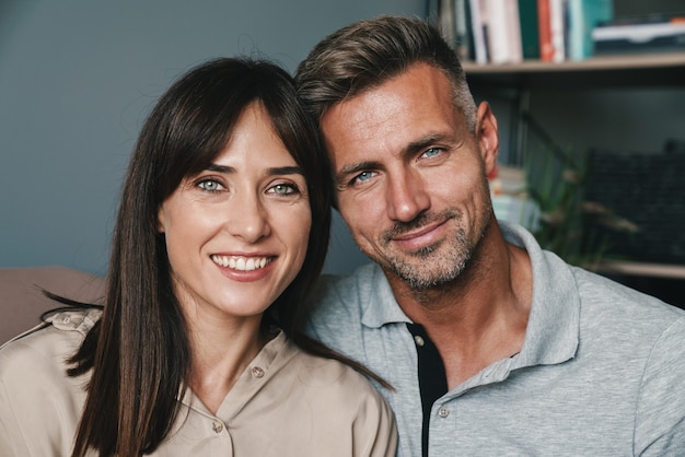 Photo d'un couple caucasien adulte homme et femme souriant tout en se blottissant sur un canapé à la maison