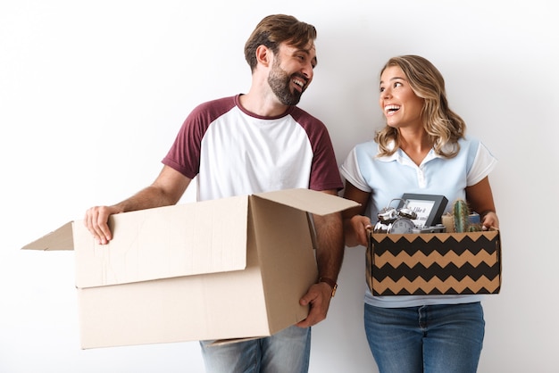 Photo d'un couple drôle dans des vêtements décontractés tenant des boîtes en carton tout en se regardant isolé sur un mur blanc