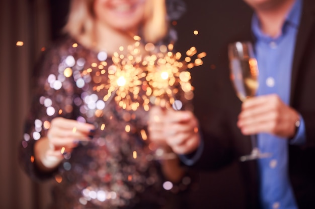 Photo d'un couple heureux avec des verres de champagne et des cierges magiques sur fond noir