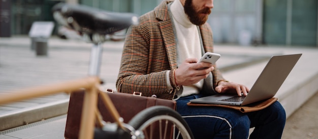 Photo de couverture Coupe médiane d'un homme assis à l'extérieur avec un ordinateur portable et un téléphone portable Appel en ligne Travailler à l'extérieur