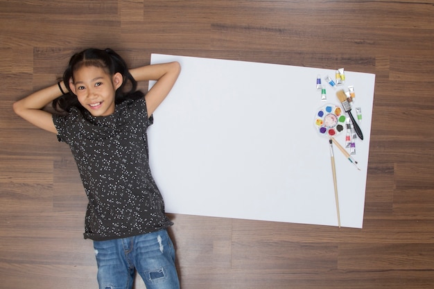 Photo créative vue de dessus de fille sur le plancher en bois. avec pinceau peinture dessin papier à colorier