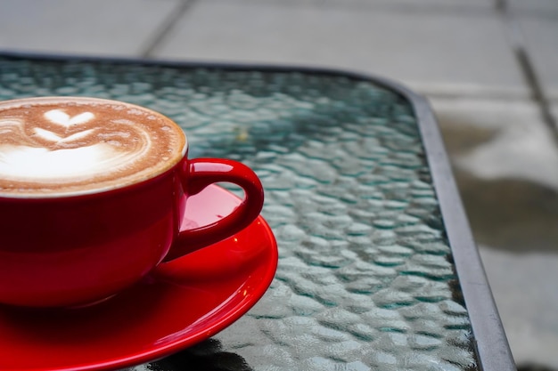 Une photo d'une demi-tasse de cappuccino. Cappuccino dans une tasse rouge servi sur une table en verre