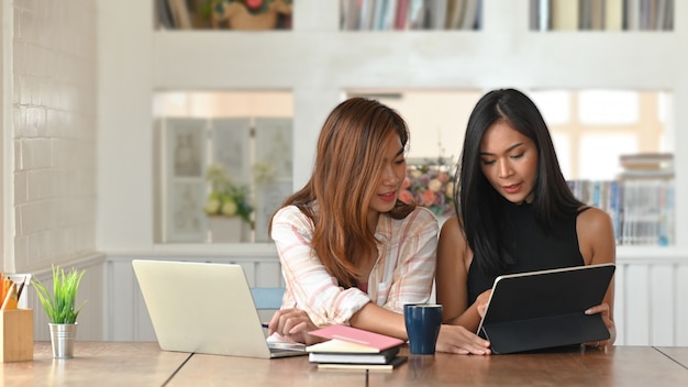 Photo de deux belles femmes pendant le tutorat d'une leçon d'étude de l'université à la table en bois moderne