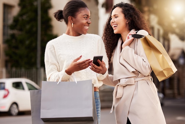 Photo de deux jeunes femmes utilisant un smartphone lors de leurs achats dans un contexte urbain