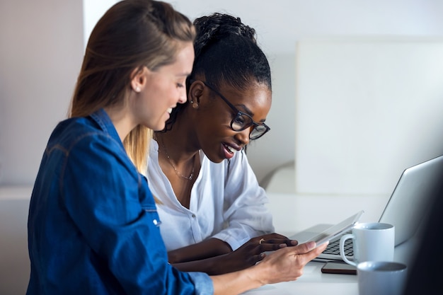 Photo de deux jolies jeunes femmes d'affaires travaillant avec une tablette numérique au bureau.