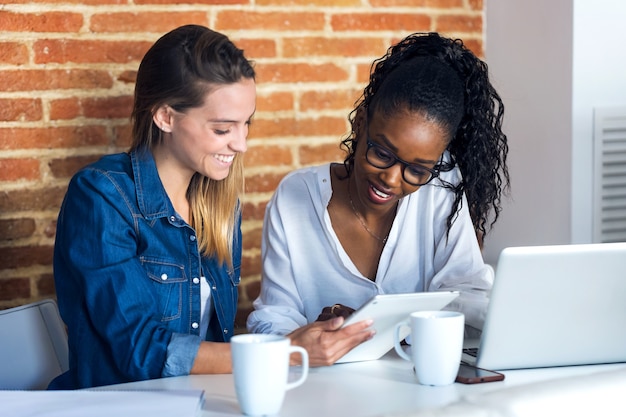 Photo de deux jolies jeunes femmes d'affaires travaillant avec une tablette numérique au bureau.