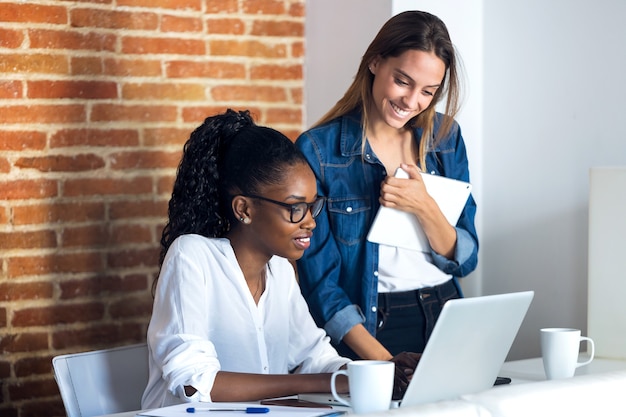 Photo de deux jolies jeunes femmes d'affaires travaillant avec une tablette numérique et un ordinateur portable au bureau.