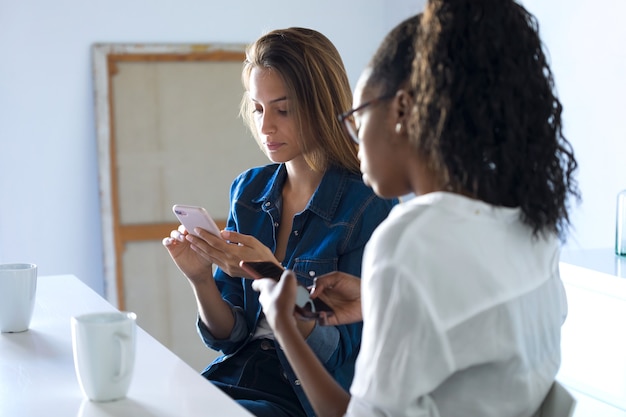 Photo de deux jolies jeunes femmes d'affaires utilisant leur téléphone portable au bureau.