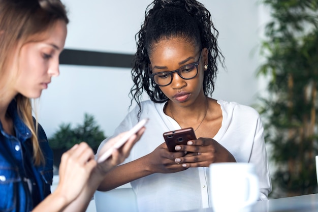 Photo de deux jolies jeunes femmes d'affaires utilisant leur téléphone portable au bureau.