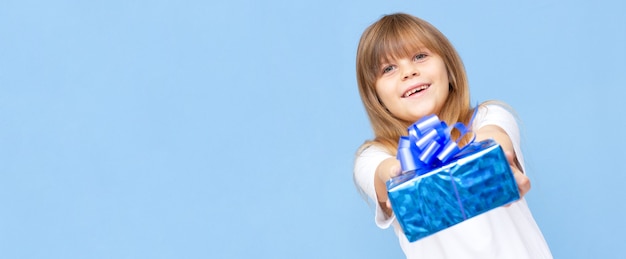 Photo D'une Douce écolière Mignonne Portant Un T-shirt Blanc Souriant Tenant Une Boîte Présente Bleue Isolée Fond De Couleur Bleue Bannière Copie Espace