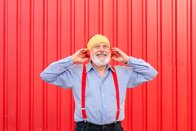 Photo d'un drôle d'homme retraité souriant touchant des écouteurs écouter de la musique isolé sur fond rouge