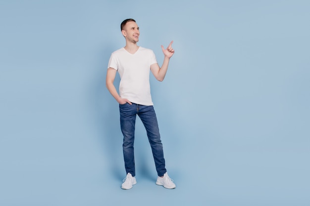 Photo du corps entier du jeune homme heureux smiel positif regarder indiquer l'espace vide du doigt annonce sélectionnez suggérer isolé sur fond de couleur bleu