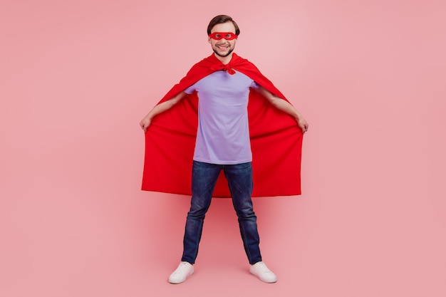 Photo du corps entier du jeune superman fort pouvoir porter un masque de manteau confiant isolé sur fond de couleur rose