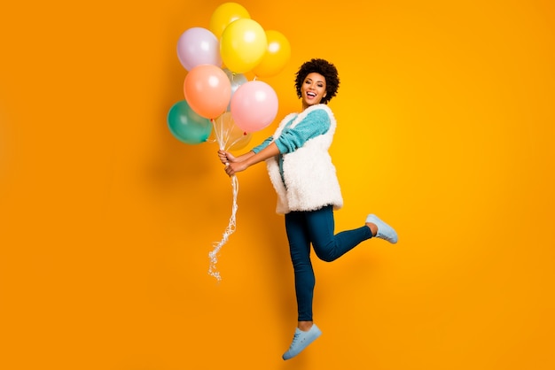 Photo du corps entier émotions positives fille afro-américaine hipster jump hold baloons anniversaire porter blanc élégant chandail sarcelle à la mode pantalon bleu pantalon chaussures isolé mur de couleur vive