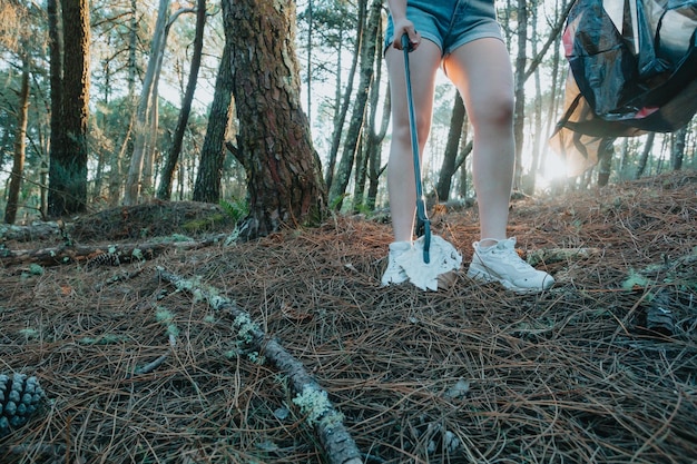 Photo du côté d'une fille ramassant des ordures dans un sac sur la forêt pendant un coucher de soleilPollution des ordures environnementalesNettoyage de la nature volontaire écologie concept vert