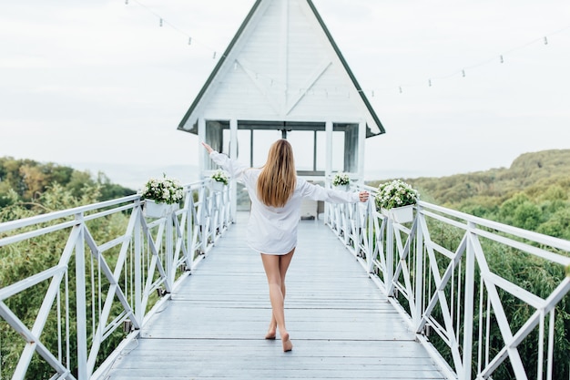 Photo du dos. Matin de la mariée, jolie fille en chemise d'homme sur la terrasse d'été.