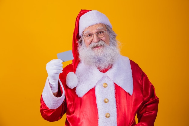 Photo du Père Noël tenant une carte de crédit sur fond jaune. Concept de paiement facile avec carte de crédit ou de débit. paiement bancaire