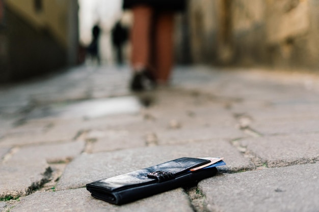 Photo du trottoir et des jambes d'un homme qui a perdu son portefeuille en cuir noir en marchant