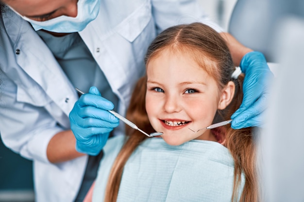 Photo d'un enfant souriant lors d'un rendez-vous chez le dentiste Un médecin portant des gants tient des outils d'examen derrière la dentisterie pour enfants