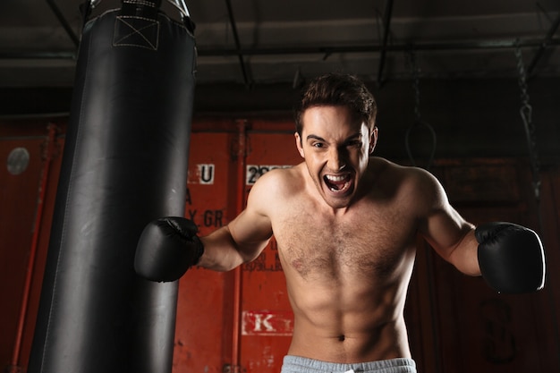 Photo d'un entraînement de boxeur agressif hurlant dans une salle de sport avec sac de frappe.