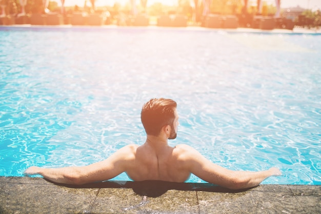 Photo d'été d'un homme souriant musclé dans la piscine. Modèle masculin heureux dans l'eau pendant les vacances d'été.