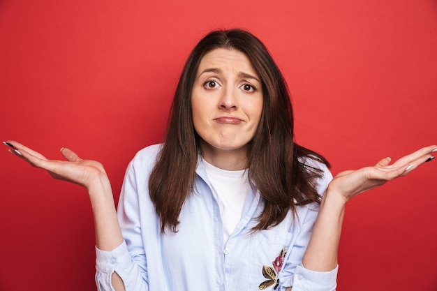 Photo d'une étonnante jeune belle femme confuse posant isolée sur un mur rouge.