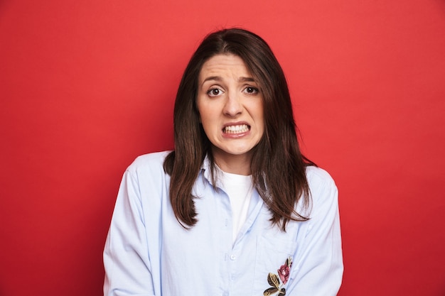 Photo d'une étonnante jeune belle femme confuse posant isolée sur un mur rouge.