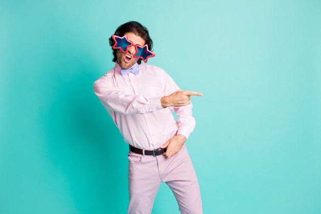 Photo d'un étudiant aux cheveux ondulés brun mignon habillé en tenue rose dansant pointant un doigt vers l'espace vide isolé sur fond de couleur turquoise