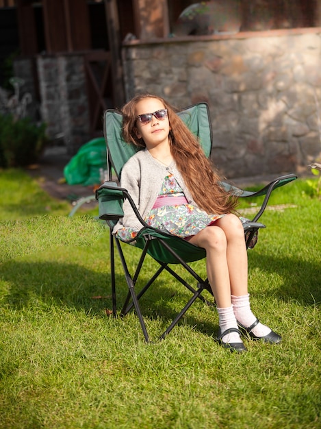 Photo extérieure d'une jolie fille prenant un bain de soleil sur une chaise sur l'herbe