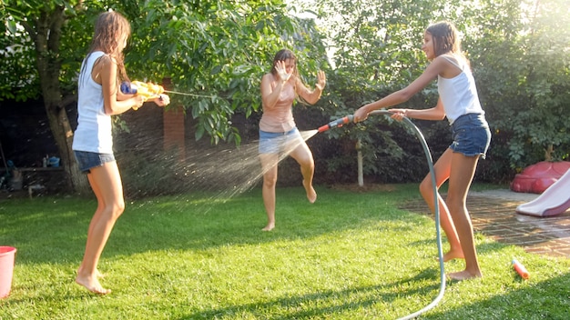 Photo d'une famille heureuse qui rit aux éclaboussures d'eau avec des pistolets à eau et un tuyau d'arrosage dans la cour. Les gens jouent et s'amusent par une chaude journée d'été ensoleillée