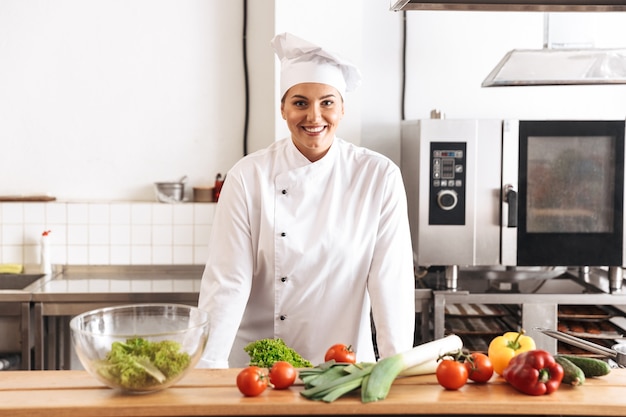 Photo de femme adulte chef vêtu d'un uniforme blanc cuisine repas avec des légumes frais, dans la cuisine au restaurant