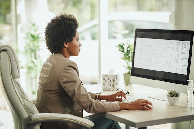 Photo d'une femme d'affaires africaine assise seule dans son bureau à domicile et travaillant sur ordinateur pendant la pandémie du virus corona.