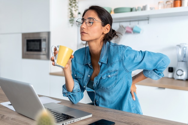 Photo d'une femme d'affaires fatiguée souffrant de maux de dos semblant mal à l'aise lorsqu'elle travaille à domicile sur un ordinateur portable.