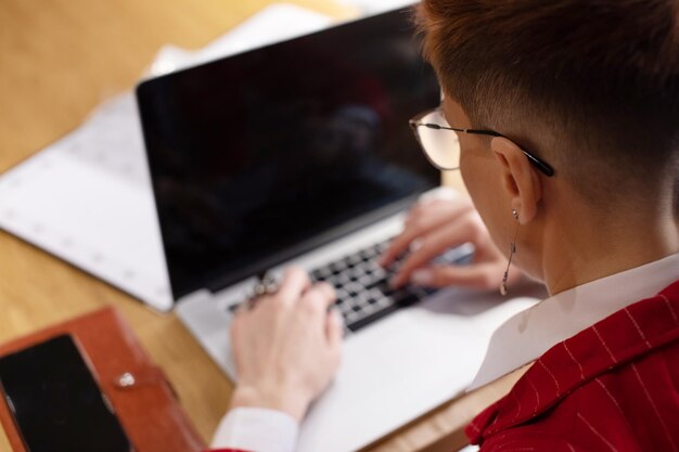 Une photo d'une femme d'affaires mature et attrayante en costume rouge travaillant sur un ordinateur portable dans son poste de travail