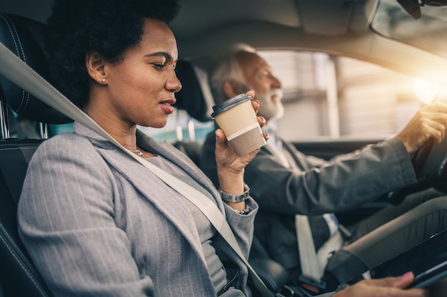 Photo d'une femme d'affaires noire prospère buvant du café pour aller et utilisant une tablette numérique pendant son trajet du matin.