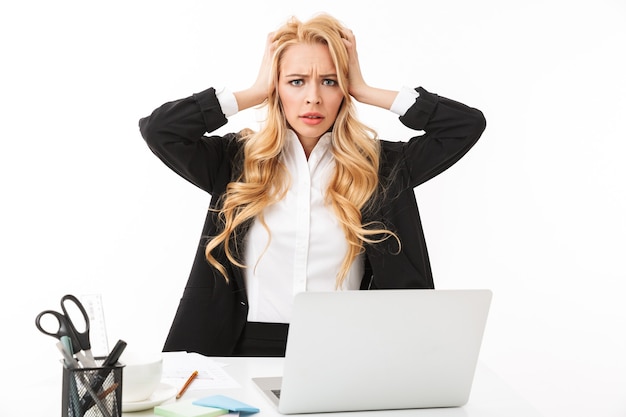 Photo de femme d'affaires perplexe assis à table et travaillant sur ordinateur portable, isolé