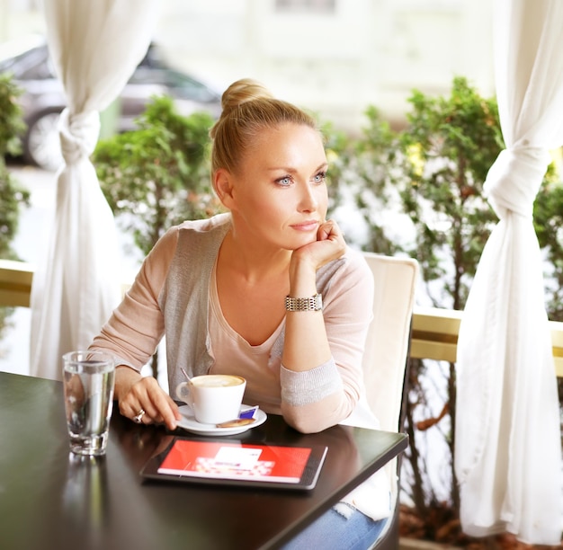 Photo d'une femme d'âge moyen utilisant une tablette numérique assise dans un café en plein air