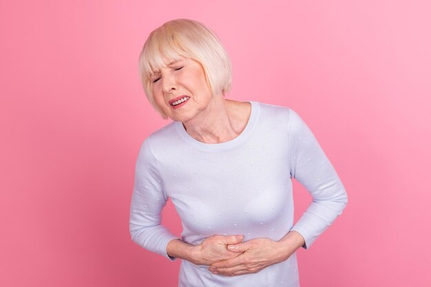 Photo d'une femme âgée mains sur l'estomac manger des spasmes d'infection alimentaire avariée isolés sur fond de couleur rose